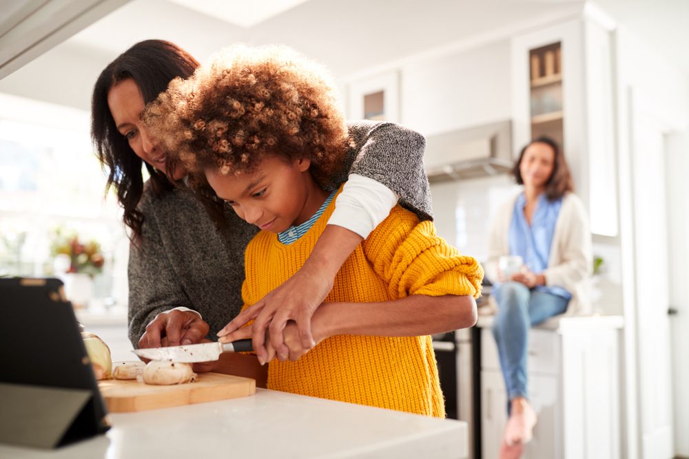 Grandmother teaching grandkid to cut up vegetables.