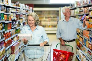 Senior couple shopping for groceries, carrying baskets and pushing carts.