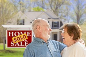 Happy couple in front of house and sign.