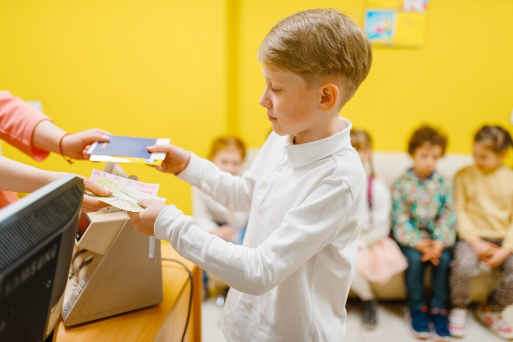Little boy buying ticket in playroom. Male kid with money paying at the cash register, child and seller at the counter