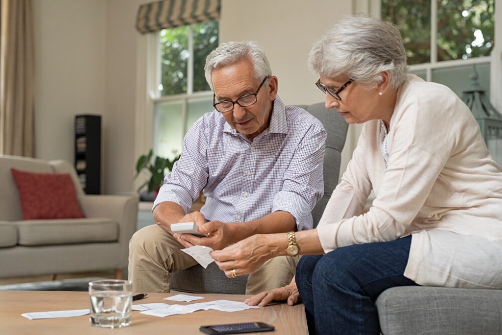 Smiling senior couple with papers, calculators and bills at home. Senior couple calculating taxes at home. Mature man and woman wearing spectacles and looking their expenses together.