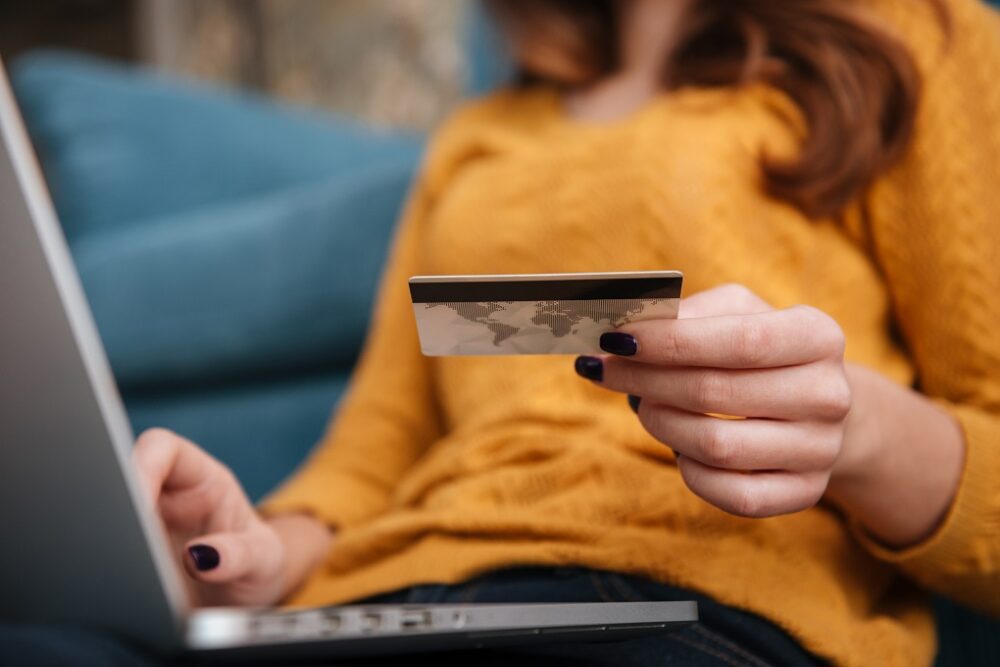 Close up of a woman buying on line with bank card and laptop while sitting in the living room at home