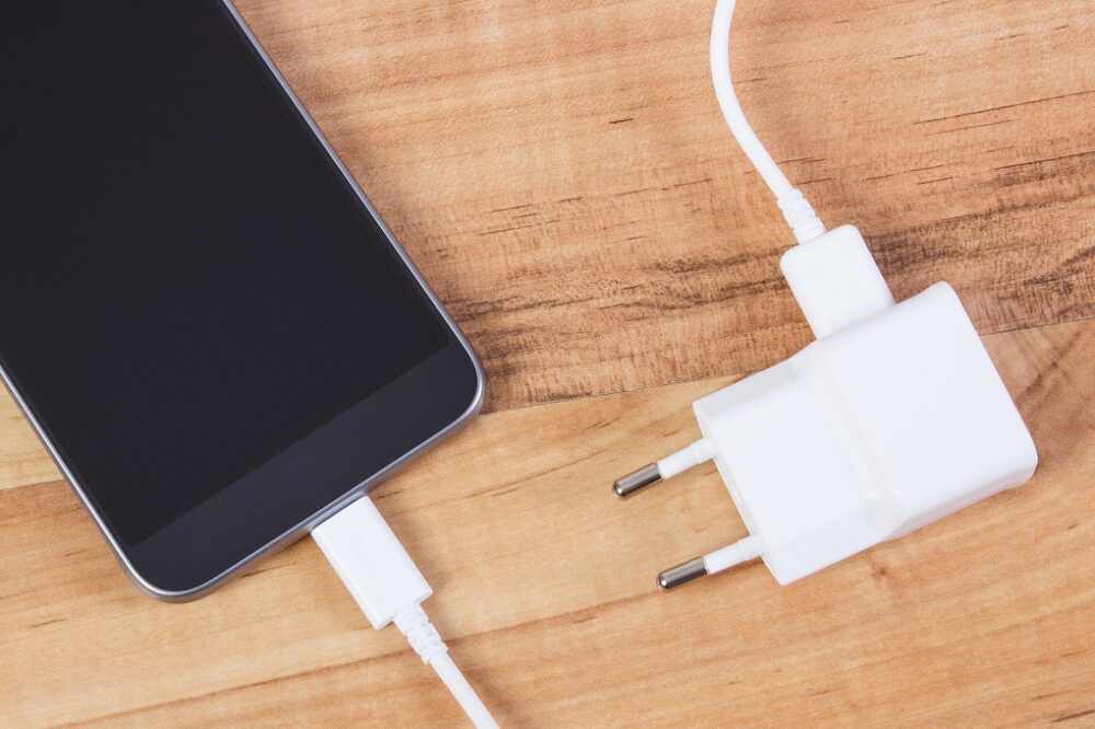 Mobile phone with connected plug of charger, smartphone charging on table