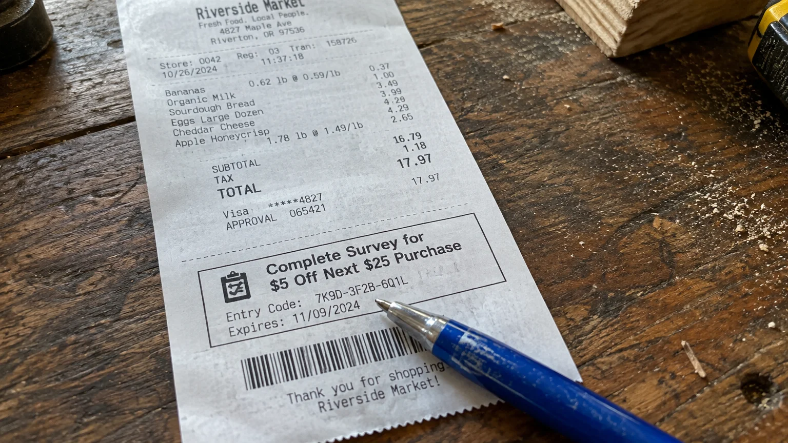 A grocery receipt with a survey coupon offering five dollars off, resting beside a blue pen on a rustic wooden table.