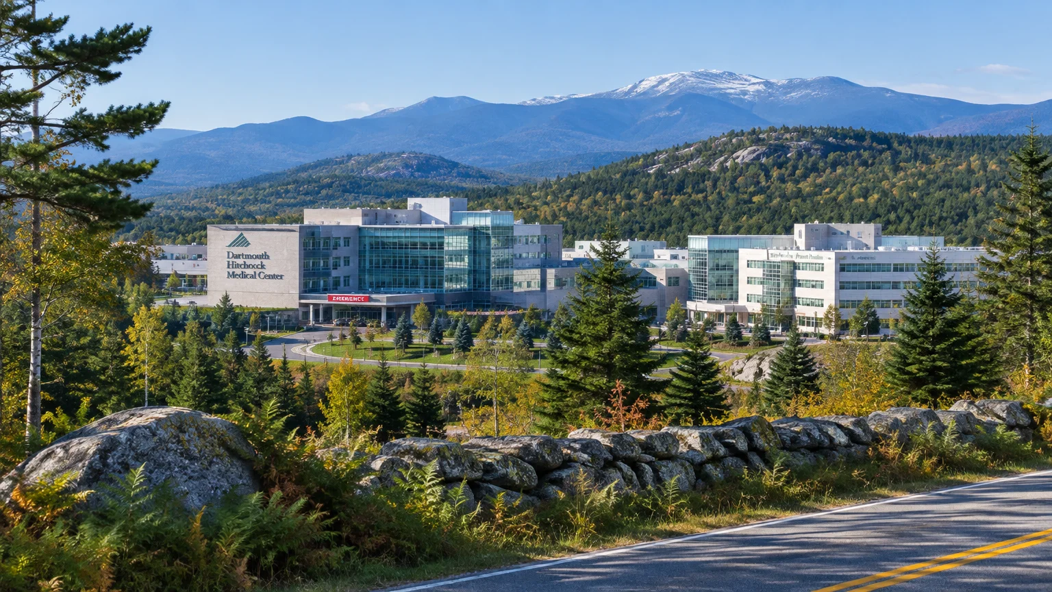Dartmouth Hitchcock Medical Center complex nestled among evergreen trees and hills with mountains in the background.