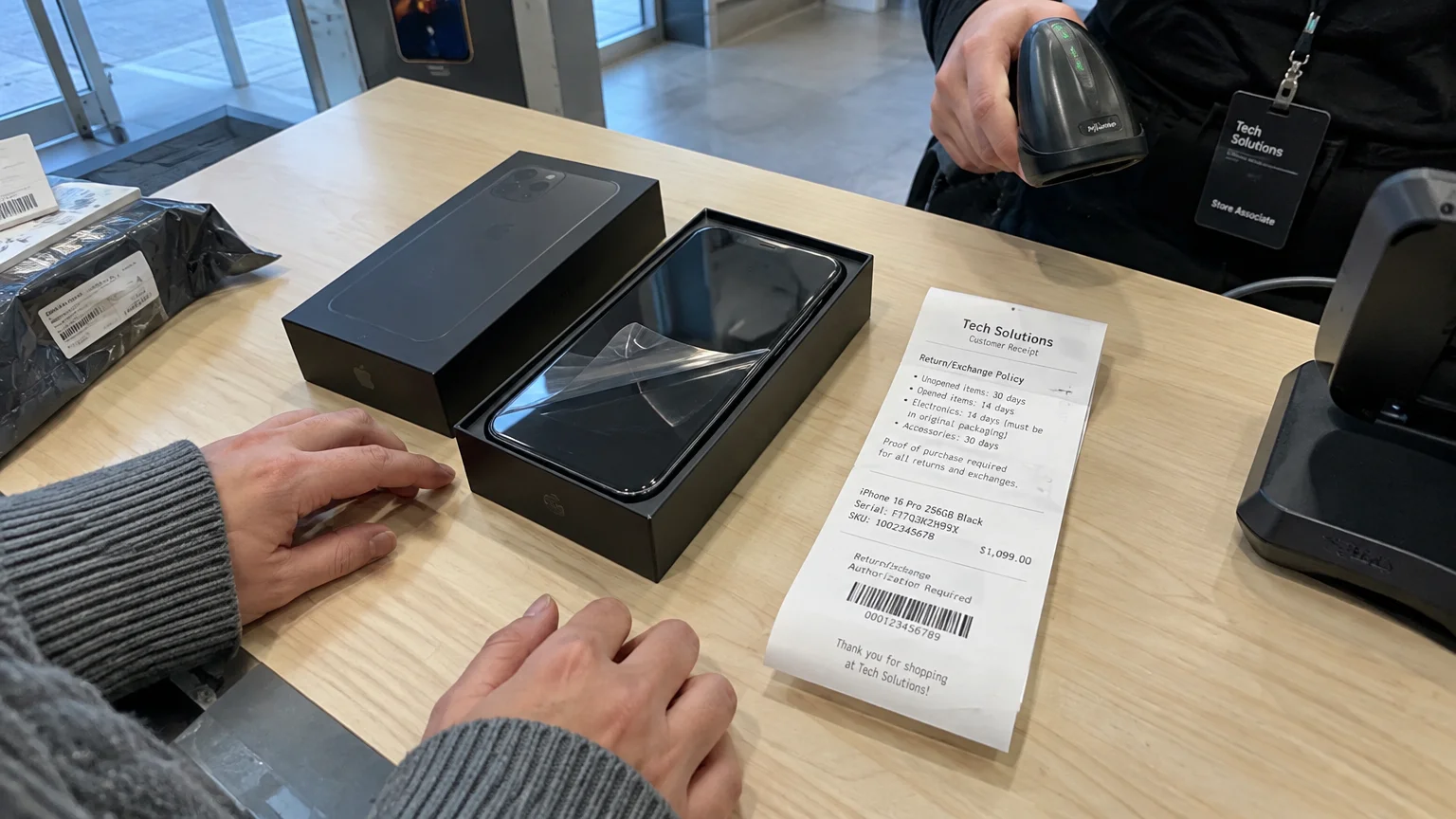 A store associate scans a receipt beside an opened smartphone in its black box on a checkout counter.